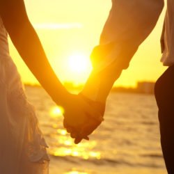 Bride and groom holding hands in front of a sunset